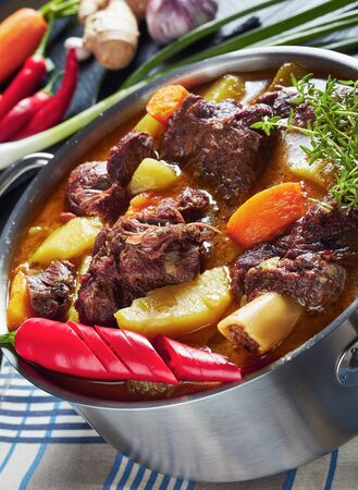 close-up of Jamaican Curry Goat â slow cooked Jamaican Spiced meat and veggies Curry in a pot on a black wooden table with ingredients on a cutting board, vertical view from above, macroの写真素材