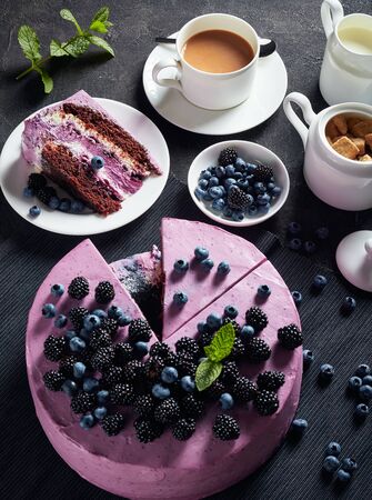 delicious blueberry and blackberries sponge cake with cream cheese  inside on a black dish on a concrete table with a cup of tea, milk in a jug and berries in a bowl.の写真素材