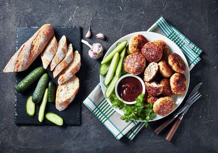 overhead view of Polish Meat cakes served with cucumber slices and barbeque sauce on a white plate on a concrete table with sliced french baguette, horizontal view from above, flatlay, copy spaceの写真素材
