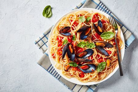 close-up of pasta with mussels in a Spicy Tomato Sauce on a white plate on a white concrete table, horizontal view from above, empty spaceの写真素材