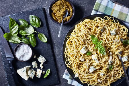 close-up of Spaghetti with genovese basil pesto and blue cheese on a black plate on a concrete table with ingredients on a slate plate, view from above, flatlay,の写真素材