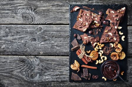 homemade chocolate bar with dried figs and cashew filling on a black slate tray with ingredients, horizontal view from above, flatlay, empty spaceの写真素材