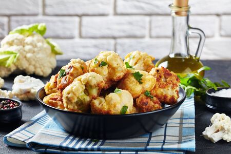 Cauliflower florets fried in batter served in a bowl on a concrete table with fresh Cauliflower and bottle of olive oil at the background of a brick wall, view from above, close-upの写真素材