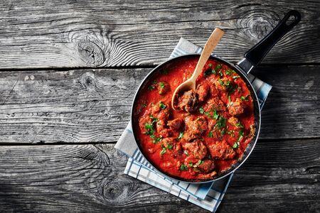 African Beef Stew in tomato sauce with spices and herbs in a skillet on an old wooden table, view from above, flatlay, empty spaceの写真素材
