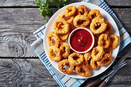 crispy calamari rings, deep-fried breaded squid rings served with tomato sauce on a white plate on an old wooden tableの写真素材