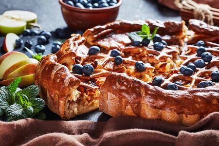 homemade delicious sliced Apple Blueberry Pie on a black slate tray on a concrete table with brown cloth and ingredients.の写真素材