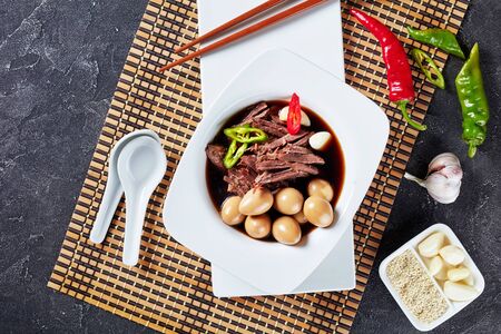 Korean food, Jangjorim, beef braised in soy sauce served in white bowl with quail eggs, garlic cloves and chili pepper slices, view from above, flatlayの写真素材