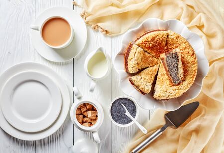 delicious sliced Poppy Seed Crumble Cheesecake on a white platter served with a cup of English tea with milk on a wooden table, horizontal view from aboveの写真素材