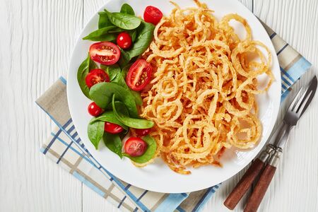 fresh spinach and tomato salad served with french crispy fried onion rings and strings on a white plate on a wooden table, view from above, flat lay, free space, close-upの写真素材