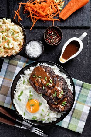 loco moco of white rice with burger patties, a fried egg, brown gravy, and macaroni salad served on a black plate on a concrete table, Hawaiian cuisine, vertical viewの写真素材