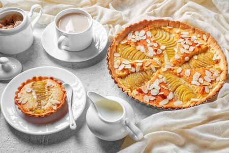 close-up of French Pear Tart, La Tarte Bourdaloue filled with poached pears and frangipane cream served on a concrete table with a cup of  cocoa drink and fresh creamの写真素材