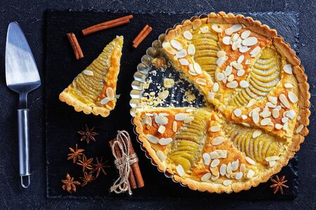 close-up of French Pear Tart, La Tarte Bourdaloue filled with poached pears and frangipane cream served on a black stone board on a concrete tableの写真素材