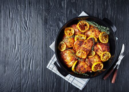 delicious Chicken Thighs With Roasted Lemon Slices and thyme in a black ceramic dish on a wooden table, horizontal view from above, flatlay, free spaceの写真素材