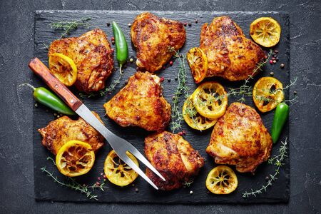 crispy fried Chicken Thighs With Roasted Lemon Slices and thyme on a black stone board on a concrete table, view from above, flatlay, close-upの写真素材