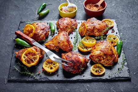 close-up of crispy fried Chicken Thighs With Roasted Lemon Slices, jalapeno peppers and thyme on a black stone tray on a concrete table, view from aboveの写真素材