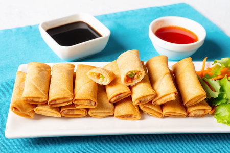 crispy bite-sized Chinese spring rolls with cabbage, carrots and green peas fillings on a white...