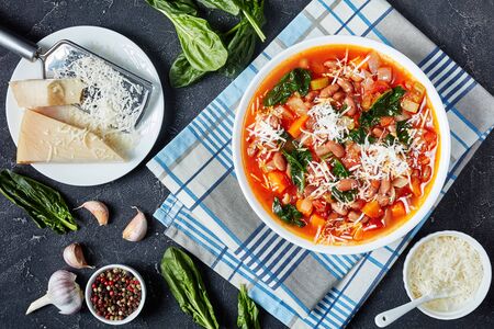 italian borlotti or cranberry beans soup with celery, vegetables, spinach, parmesan and tomatoes in a white bowl on a concrete table, horizontal view from above, flat layの写真素材