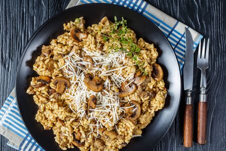 wild mushrooms Creamy risotto with grated cheese and thyme on a black plate on a wooden table, view from above, flatlay, close-upの写真素材