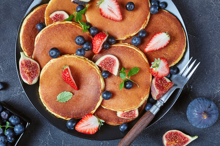 close-up of almond flour pancakes on a black plate with strawberries, blueberries, figs and mint, on...