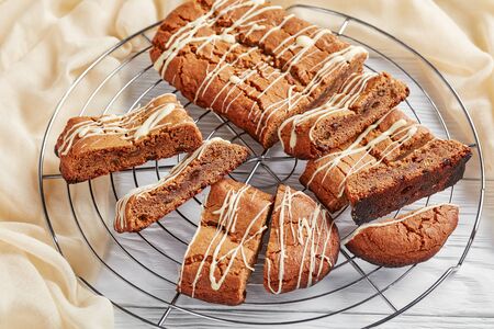 close-up of Hermit Bars, Soft and Chewy Molasses bars, classic molasses cookies with raisins, sprinkled with white chocolate sauce on a metal wire stand on a wooden table, view from aboveの写真素材