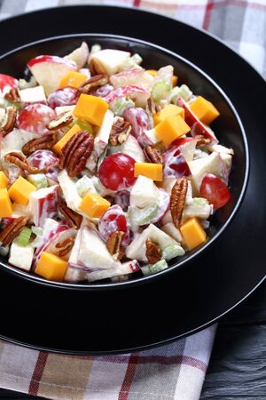 fresh apple salad with grapes, celery, cheddar cheese and pecan nuts with mayonnaise based dressing on black plates on a wooden table, vertical view, close-upの写真素材