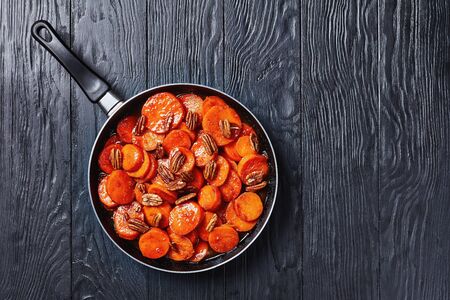 Candied sweet potatoes with brown sugar in a skillet on a black wooden tableの写真素材