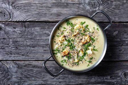 Creamy roasted garlic cauliflower soup with asiago cheese and a crunchy popped quinoa and chia seed topping in a stockpot on a rustic wooden table, horizontal view from above, flatlay, free spaceの写真素材