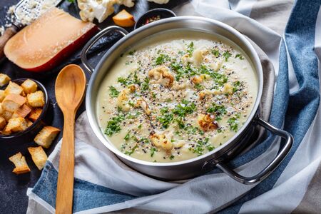 close-up of Creamy roasted garlic cauliflower soup with asiago cheese in a stockpot with ingredients and croutons on a concrete tableの写真素材
