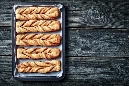 freshly baked Cinnamon sugar puff pastry twists on a pan sheet on a wooden rustic tableの写真素材
