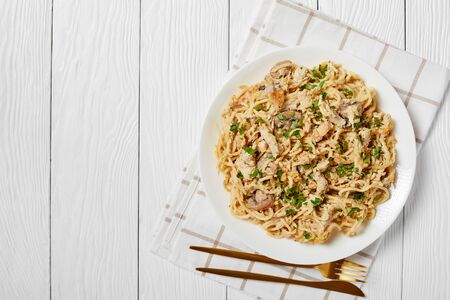 roasted turkey breast tetrazzini served on a white plate with golden fork and knife on a wooden table, american cuisine, horizontal view from above, flat lay, free spaceの写真素材