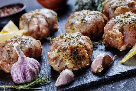 Raw rabbit ballotine prepared to be cooked on a black slate plate with herbs and spices