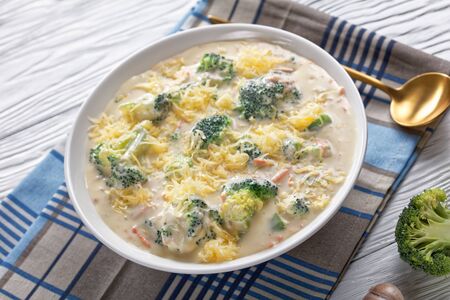 cheesy broccoli and vegetable soup in a white bowl with a golden spoon on a napkin, view from aboveの写真素材