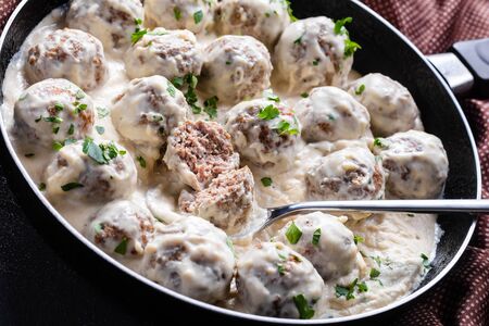 classic Swedish meatballs with creamy sauce and parsley in a skillet on a concrete kitchen table, horizontal view from above, close-upの写真素材