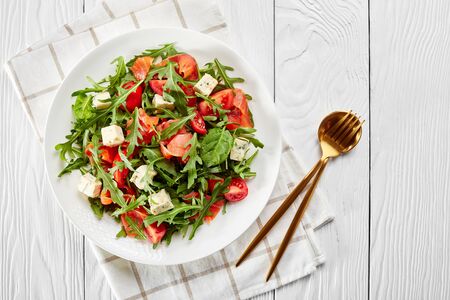 close-up of delicious healthy salmon arugula blue cheese tomato salad on a white plate with golden cutlery on a wooden table, horizontal view from above, flat lay, free spaceの写真素材