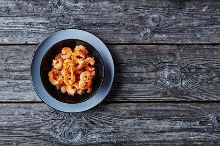 Shrimp scampi sauteed with garlic and butter sauce sprinkled with parsley served on a black plate on rustic old wooden background   horizontal orientation, view from above, copy spaceの写真素材