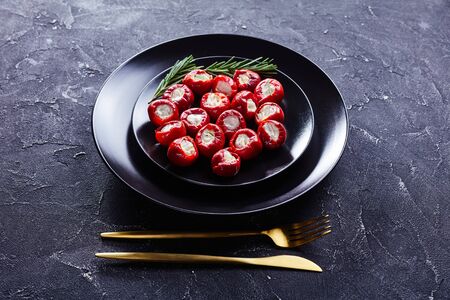 Spicy cherry peppers stuffed with soft ricotta cheese served on a black plate with rosemary sprigs with golden cutlery on a dark concreteの写真素材