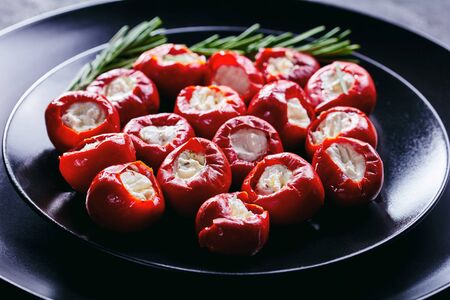 Hot red tiny cherry peppers stuffed with soft ricotta cheese served on a black plate with rosemary sprigs on a dark concreteの写真素材