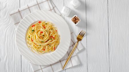 Pasta  on a white plate with golden fork and salt shaker on a wooden tableの写真素材