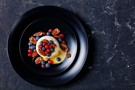 Cooked soft mold brie with pecan, blueberries, cranberries, and honey on top served on a black plate on a dark concreteの写真素材