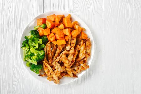 Skinny chicken and veggies platter with sweet potato, grilled chicken and boiled broccoli on a white plate on a white wooden top view, horizontal orientation, close-upの写真素材