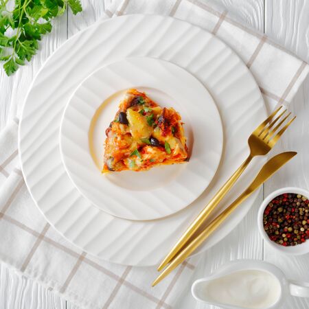 Baked chicken tamale pie or chicken casserole with a cornmeal mix crust, cheddar cheese, black beans served on a plate with sour cream on a white wooden background, view from above, close-upの写真素材
