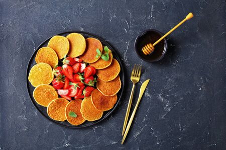oatmeal gluten free pancakes with strawberries and honey on a black plate on a concrete table, healthy food, horizontal view from above, free space, flat layの写真素材