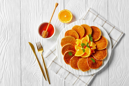 oatmeal sweet pancakes with orange and honey on a white plate on a wooden table with golden fork and knife, healthy food, horizontal view from above,  flat lay, free spaceの写真素材