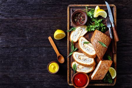 Baked Omelet Roll with chicken minced meat on a rude rustic wooden tray served with lemon, tomato sauce and mustard on a wooden table, horizontal view from above, flat lay, free spaceの写真素材