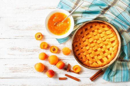 sweet apricot pie with a lattice pie crust topping in a baking shell with fresh apricots and kitchen towel on a rustic wooden table, flat lay, free spaceの写真素材