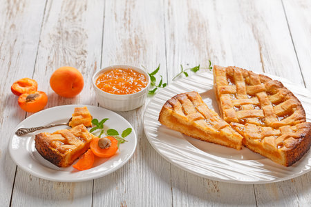 close-up of sliced apricot shortcrust pie with a lattice pie crust topping on white plates on a rustic wooden table, landscape view, free spaceの写真素材