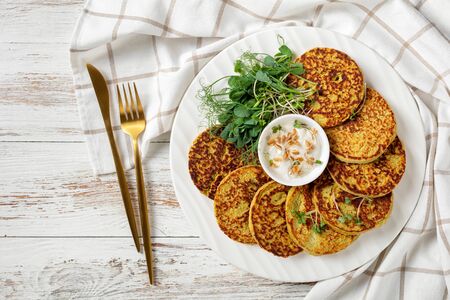 green pea and oatmeal pancakes on a white platter with plain greek yogurt sauce with fresh sprouts of pea and wheat, healthy diet concept, horizontal view from above, flat lay, close-upの写真素材