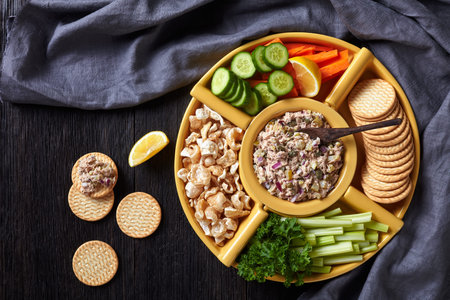 Tuna capers pickles Spread set served with carrots and celery sticks, sliced fresh cucumber, crackers and pork rinds in bowls on a dark wooden table, Philippines cuisine, flat lay, free spaceの写真素材