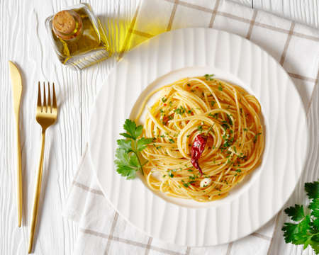 Spaghetti Alla colatura di alici, Spaghetti with anchovy sauce, pimento pepper, garlic and parsley on a white plate on a white wooden table, horizontal view from above, flat layの写真素材