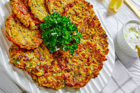 Jewish food: sweet onion latkes or pancakes with greens and rice, served on a white plate with parsley and yogurt sauce on a white wooden background, with lemon, close-upの写真素材